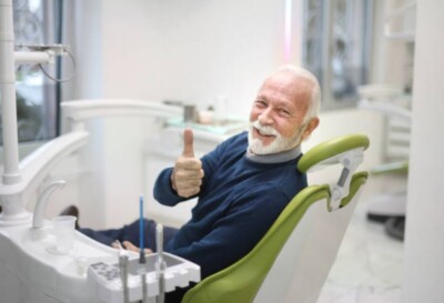 Man with grey hair in dental chair giving thumbs up